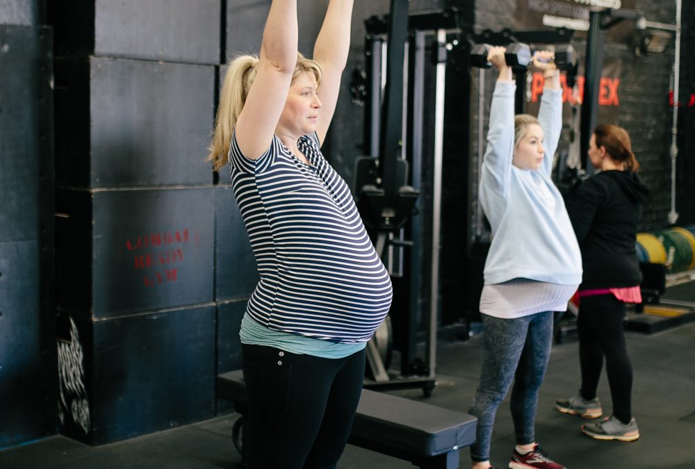 two pregnant women lifting handweights above their heads in the gym