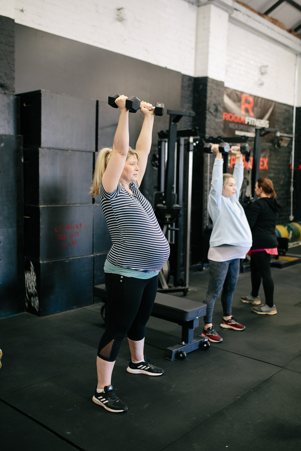 two pregnant women lifting handweights above their heads in the gym